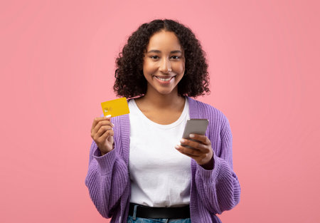 Young Black Woman Shopping Online With Cellphone and Credit Card Against a Pink Background