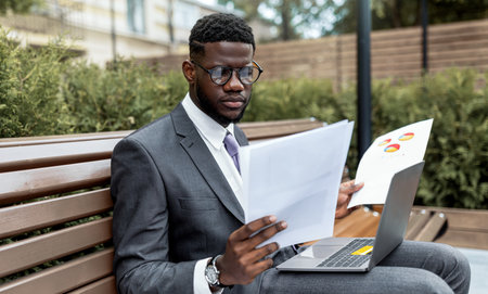 Business Professional Reviewing Documents Outdoors in a Park on a Sunny Dayの写真素材