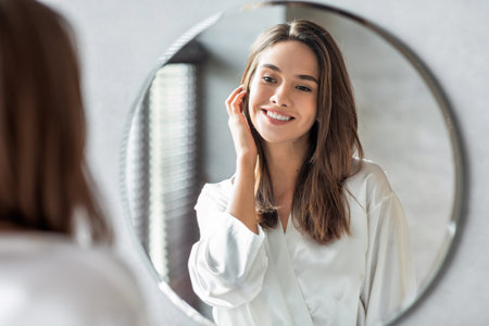 Attractive Woman Enjoys Her Reflection in the Bathroom Mirror While Wearing a Silk Robeの写真素材