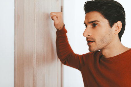 Man Waiting by a Door With a Serious Expression While Knocking Softlyの写真素材
