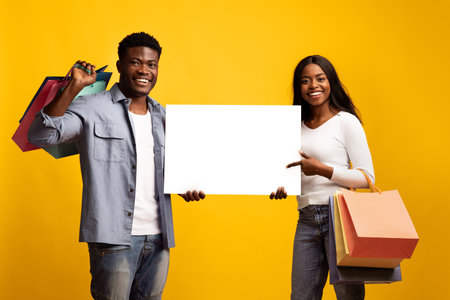 Happy Couple With Shopping Bags Poses With Blank Sign in Bright Studio Settingの写真素材