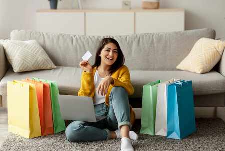 Excited Woman Enjoys Big Online Sale With Laptop and Credit Card While Surrounded by Gift Bagsの写真素材
