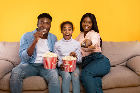 Emotional Family of Three Enjoys Movie Night Together With Popcorn on Cozy Couchの写真素材