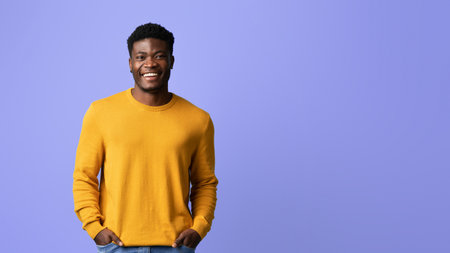 Happy Young Man in a Yellow Sweater Smiling Against a Purple Backgroundの写真素材