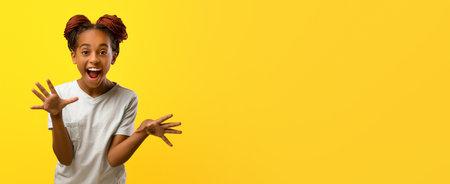 Excited Child Expresses Joy With Playful Hand Gestures Against a Bright Yellow Backgroundの写真素材