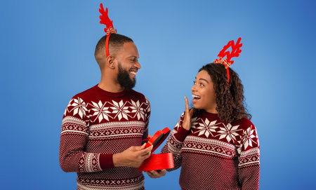 Happy black man giving gift box to surprised wife and celebrating New Year or Christmas togetherの写真素材