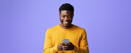 Young Man Smiling While Using Smartphone Against a Purple Background