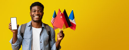 Smiling Man Holds Phone and Flags of Multiple Countries Against Yellow Backgroundの写真素材