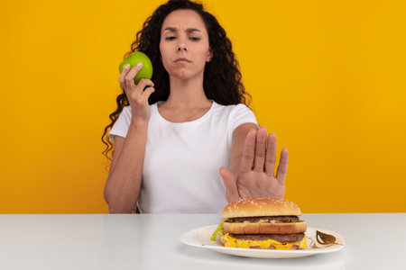 Pensive Lady Deciding Between a Burger and an Apple at a Bright Tableの写真素材