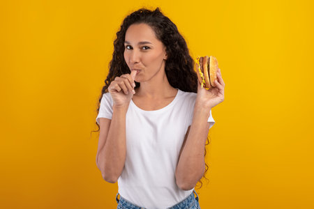 Happy Latin Woman Enjoying a Big Juicy Burger in a Studio Setting With Vibrant Yellow Background