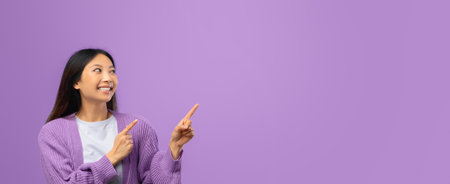 Smiling Woman in a Purple Sweater Pointing at a Blank Space on a Purple Backgroundの写真素材