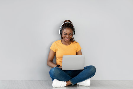 Positive Young Black Woman Working on Laptop While Sitting Cross Legged on Floorの写真素材