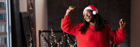 Young Woman Wearing a Santa Hat Dances Joyfully in a Festive Setting With Holiday Decorationsの写真素材