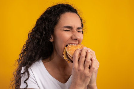 Hungry Woman Enjoys Big Burger in Studio With Yellow Background