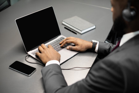 Unrecognizable black businessman using laptop with empty screen and headsetの写真素材