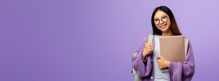Smiling Student With Glasses Shows Thumbs up While Holding Books in a Purple Backgroundの写真素材