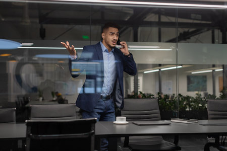 Furious Businessman Gesturing While Talking on Phone in Modern Office Settingの写真素材