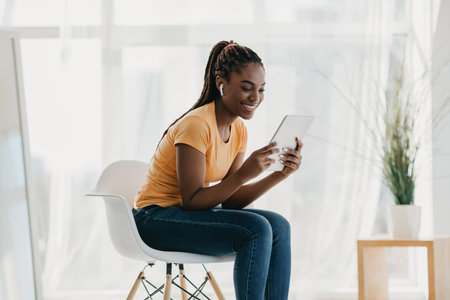 Happy Young Black Woman Enjoys Movies at Home With Wireless Earphones and Tabletの写真素材