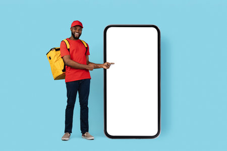 Order Here. Happy Black Delivery Guy Pointing At Big Blank Smartphone Screenの写真素材