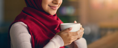 Woman Enjoys a Warm Beverage While Wearing a Red Hijab in a Cozy Indoor Settingの写真素材
