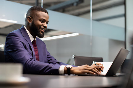 Cheerful african american entrepreneur signing papers, working on laptopの写真素材