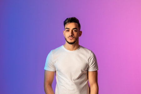 Handsome Young Man Poses Under Neon Lights With Serious Expression in Casual Attireの写真素材