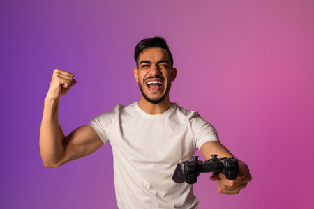 Young Arab Man Celebrates Video Game Win With Joy and Excitement in Neon Lightsの写真素材