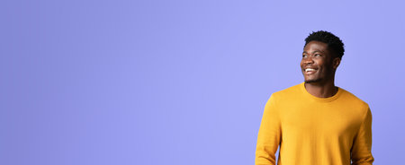 Smiling Man in Yellow Sweater Against Purple Background During Cheerful Momentの写真素材