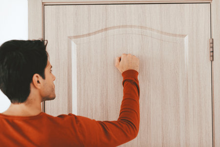 Man Knocking on Wooden Door in a Cozy Indoor Settingの写真素材