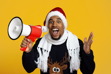 A Cheerful Man Wearing a Santa Hat and a Cozy Sweater With a Reindeer Design Holds a Megaphoneの写真素材
