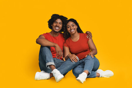 A Young Couple Sits on the Floor Against a Vibrant Yellow Backdrop