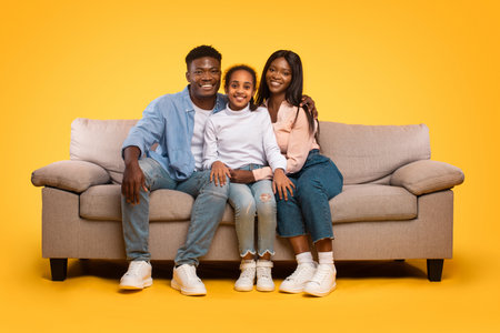 Joyful Family Sitting on Couch Together, Embracing and Smiling Against Bright Yellow Backgroundの写真素材