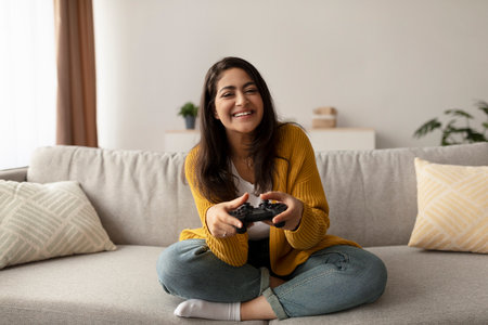 Joyful Middle Eastern Woman Enjoying Video Games on a Cozy Couch at Homeの写真素材