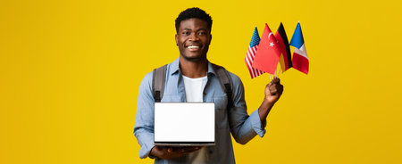 Young Man Holds Flags and Laptop in Front of Yellow Background During a Cheerful Momentの写真素材