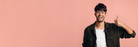 Young Man Smiling and Giving a Thumbs up Against a Pastel Pink Backgroundの写真素材