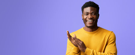 Young Man Smiles and Claps With Joy Against a Purple Backdrop in a Casual Setting