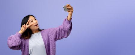 Young Woman Happily Taking a Selfie Against a Pastel Purple Backgroundの写真素材