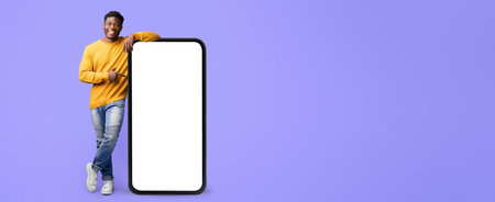 Young Man Stands Next to Large Blank Smartphone Display Against a Purple Backgroundの写真素材