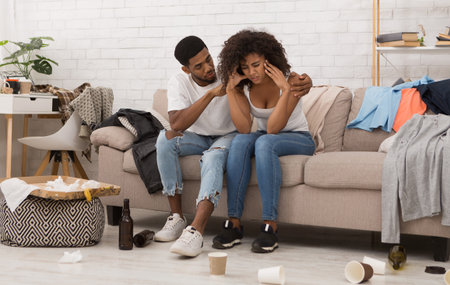 couple with hangover sitting in messy room after partyの写真素材