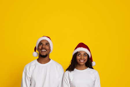 Joyful Couple Celebrating Christmas With Matching Santa Hats Against a Bright Yellow Backgroundの写真素材