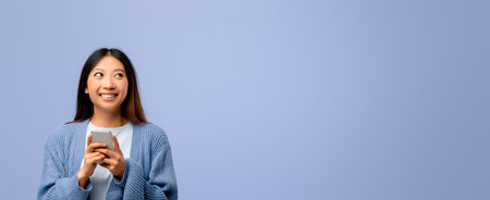 Young Woman Smiles While Holding Smartphone Against a Pastel Blue Backgroundの写真素材