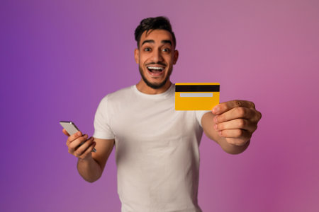 Joyful Millennial Arab Man Enjoys Online Shopping Experience With Credit Card and Phoneの写真素材