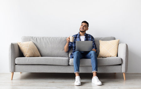 Man using pc sitting on the couch, drinking coffeeの写真素材