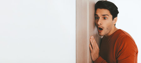 Man Showing Surprise While Peeking Around a Wall in a Modern Indoor Settingの写真素材