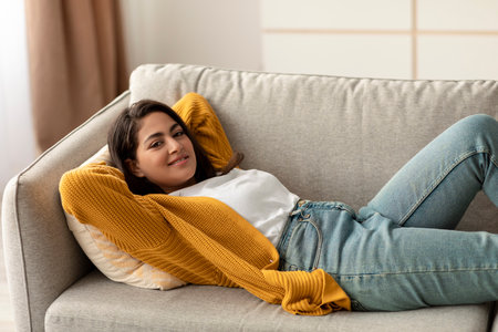 Happy Arab Woman Relaxing on a Comfortable Sofa During Her Day Offの写真素材