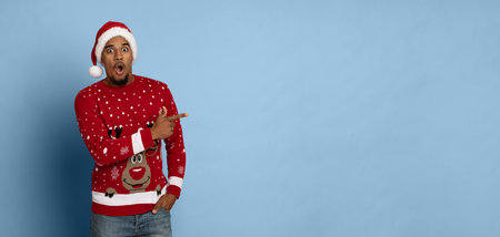 Man Wear Red Holiday Sweater and Santa Hat With Surprised Expression Against Blue Backgroundの写真素材