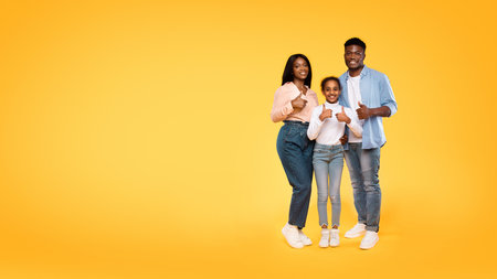 Excited Family of Three Giving Thumbs up and Smiling Against Yellow Backgroundの写真素材