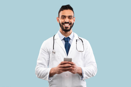 Smiling Doctor in White Coat Using Smartphone in a Bright, Simple Backgroundの写真素材