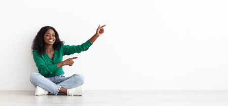 Young Woman Sitting on Floor and Directing Attention With Cheerful Expression in Spacious, Bright Interiorの写真素材