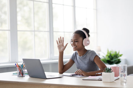 Smiling Adolescent Girl With Headphones Enjoys Video Call While Studying at Homeの写真素材
